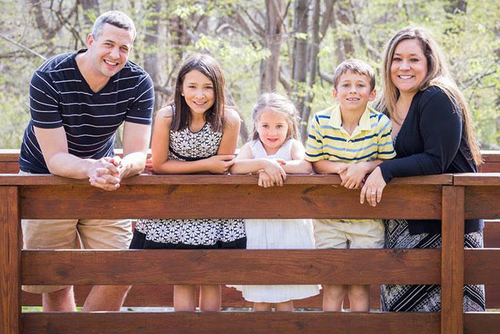 Matt Wilkes, his three children, and his wife on a bridge surrounded by trees